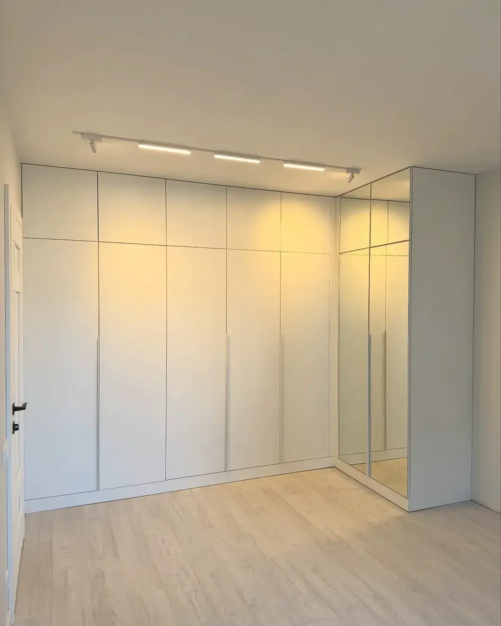 Bespoke white fitted wardrobes with a mirrored corner, built by PrimeCraft Surface Solutions in Bushey, Hertfordshire (WD23).